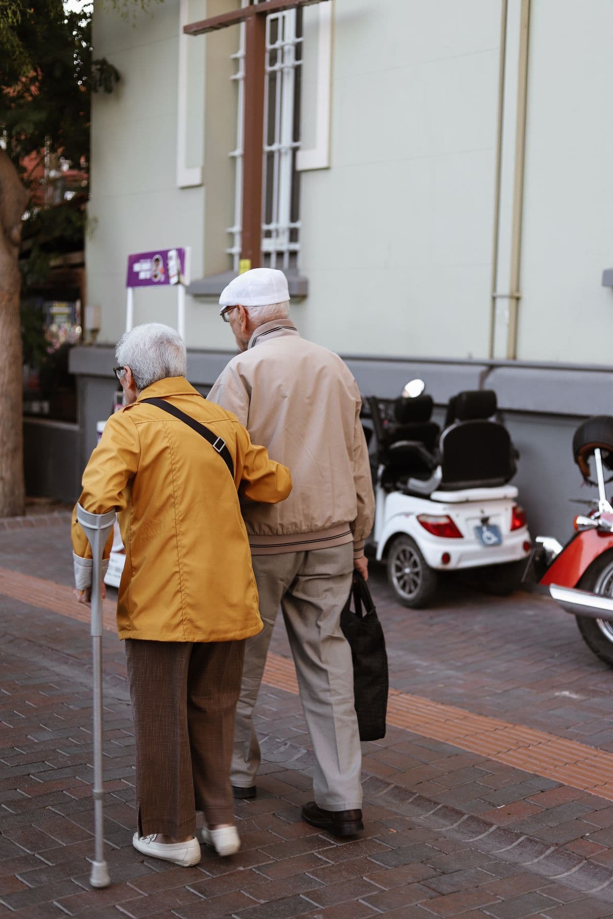 Two older people walking together down a street, seen from behind, one using a cane — illustrative demo image